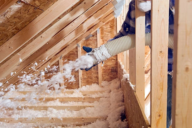 Technician installing fiberglass insulation rolls in an attic space
