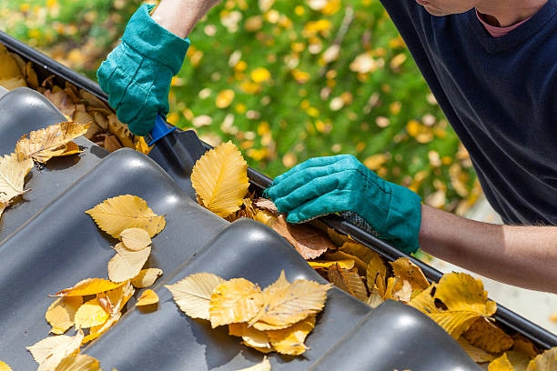 A professional performing gutter cleaning on a home in Kalamazoo, MI, removing leaves and debris to ensure proper water flow and prevent damage..